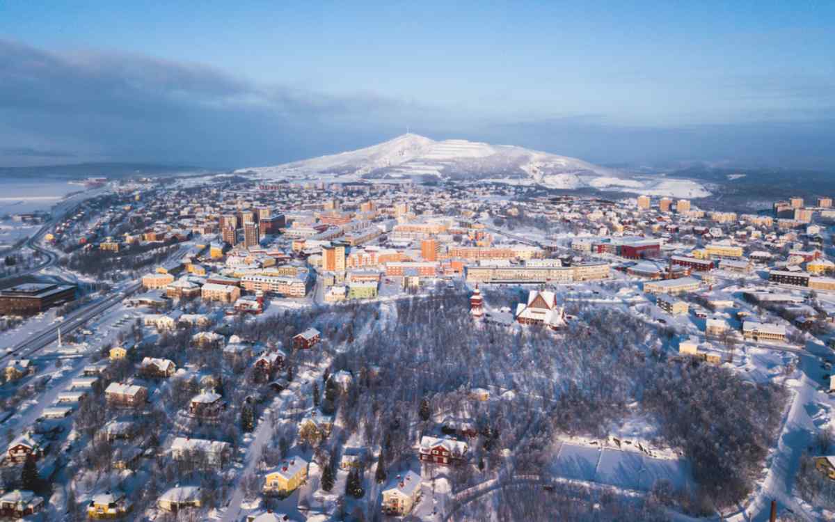 Winter aerial view of Kiruna, Sweden, with a snow-covered cityscape, Kiruna Church, and surrounding mountains in Swedish Lapland.