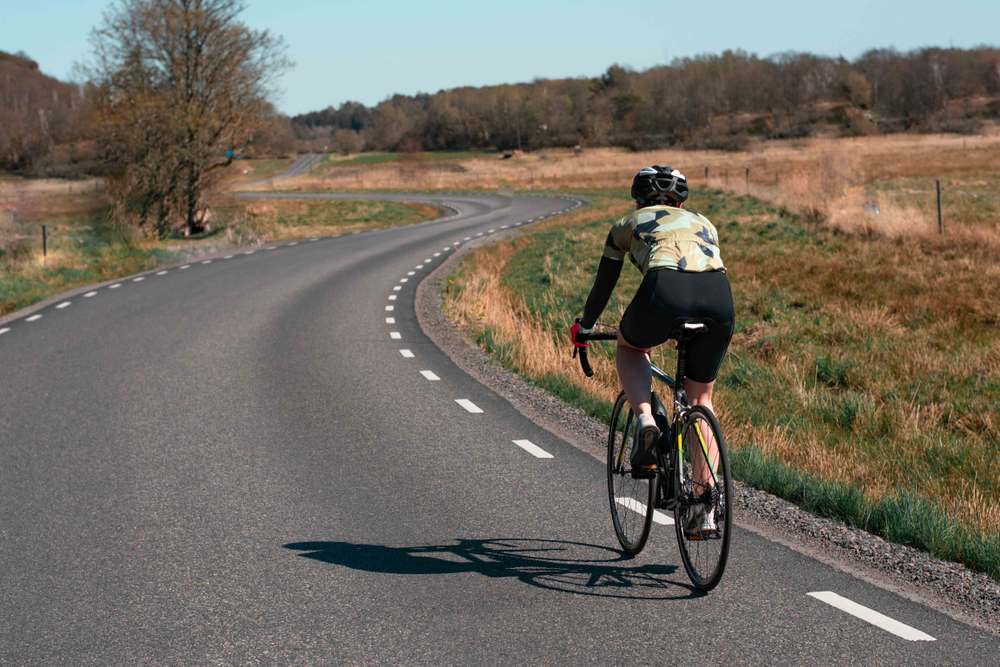 A man on his back riding a bicycle on a Swedish paved road during a sunny day and equipped to protect himself from possible falls.