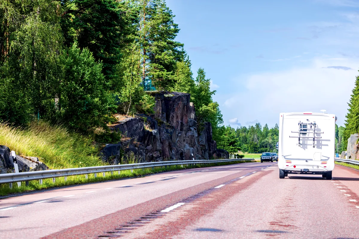 Moving to Sweden A motorhome driving on a scenic road in Sweden, surrounded by lush green trees and rocky cliffs, representing the journey of moving to Sweden.