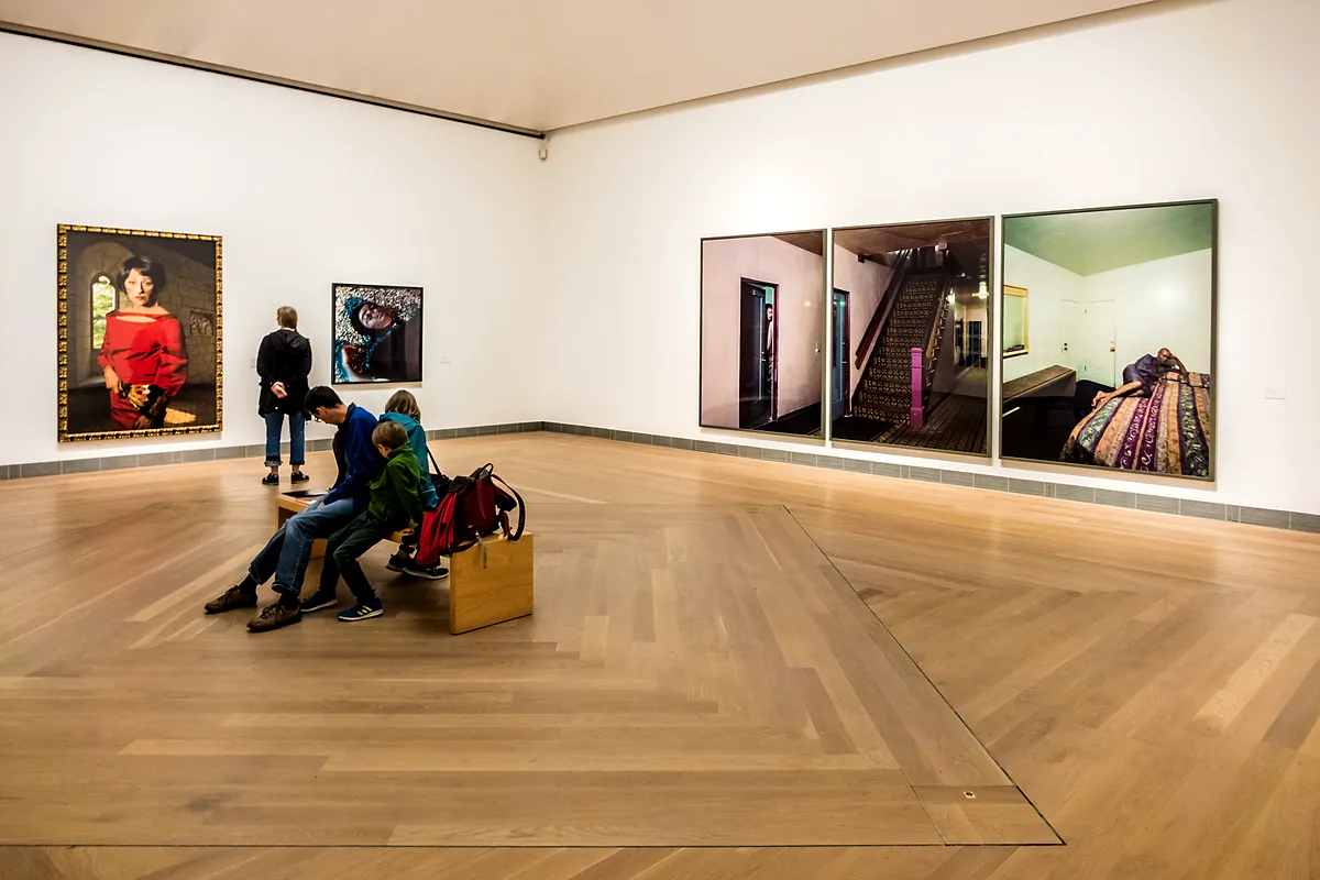 Programme des Moderna Museet Besucher des Moderna Museet beobachten zeitgenössische Kunstinstallationen in einer geräumigen Ausstellungshalle mit minimalistischen weißen Wänden, Holzböden und sanfter Beleuchtung.