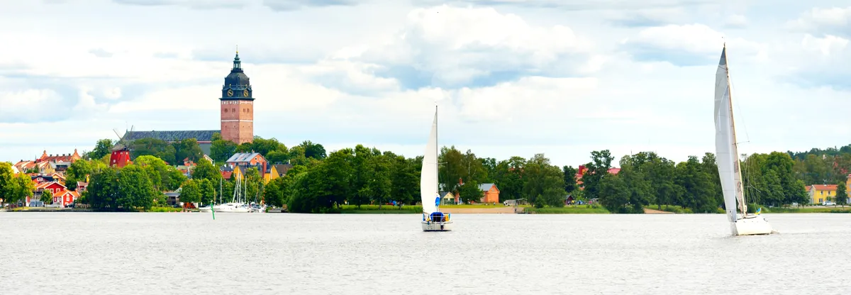 Malerische Aussicht auf Segelboote, die auf dem Mälarsee gleiten, mit der historischen Kathedrale von Västerås im Hintergrund, die natürliche Schönheit mit kulturellem Erbe verbindet.