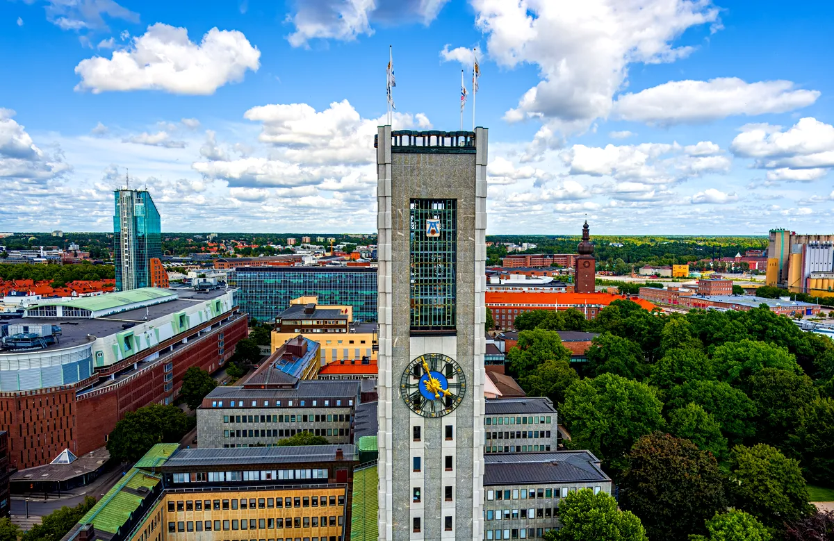 Ein Panoramablick auf Västerås, Schweden, mit dem berühmten Glockenturm der Stadt, modernen und historischen Gebäuden und Grünflächen unter einem strahlend blauen Himmel mit vereinzelten Wolken.
