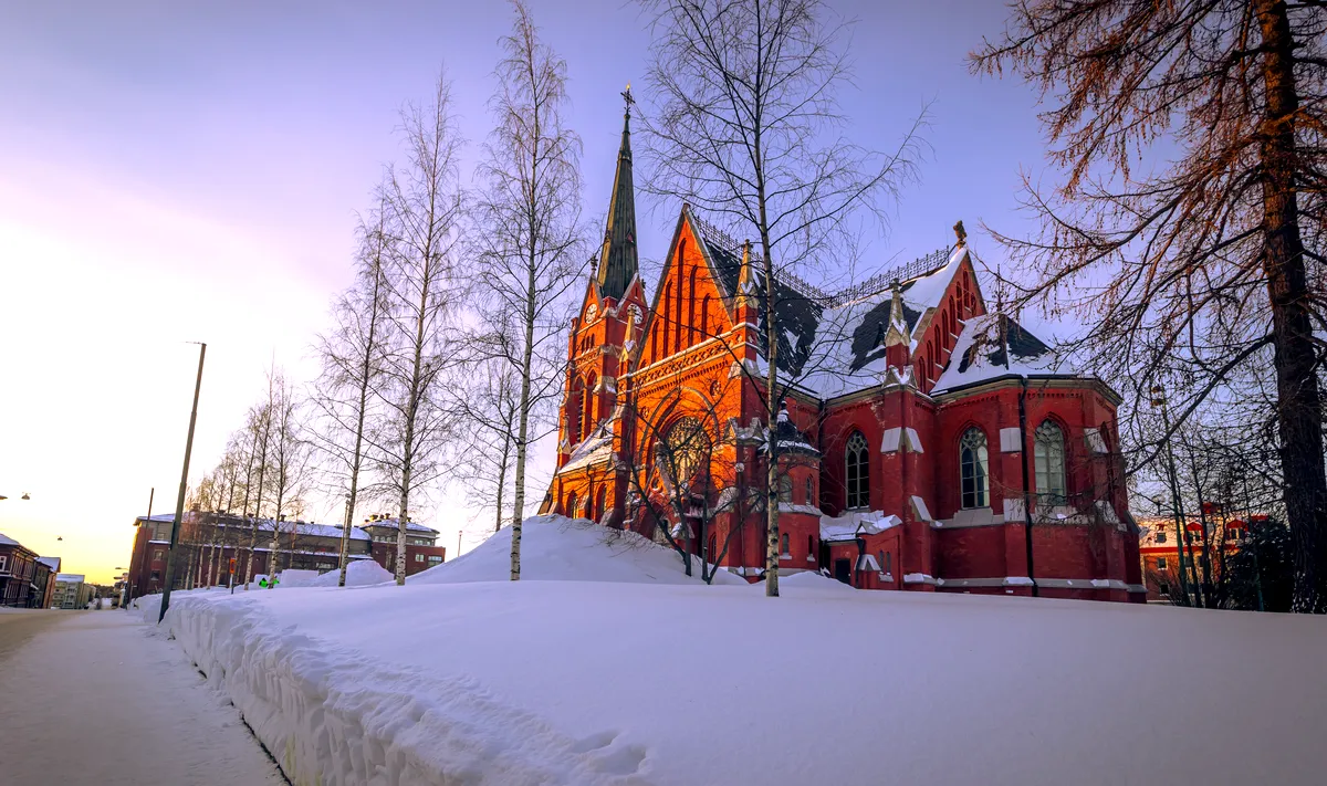 Luleå domkyrka på vintern: A Stunning Sunset Over a Historic Swedish Landmark Luleå domkyrka i Sverige under vintern, en historisk kyrka i röd tegel upplyst av solnedgången med snötäckta omgivningar.