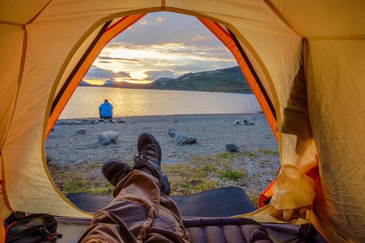 A person's legs protrude from a tent in a slightly rocky Swedish landscape near the shores of a lake.